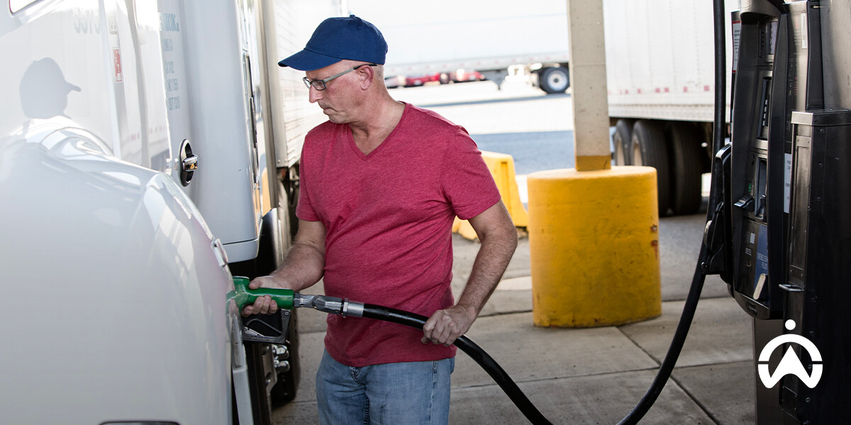 A man in a red shirt fills a large vehicle with fuel at a gas station, focusing on the pump.