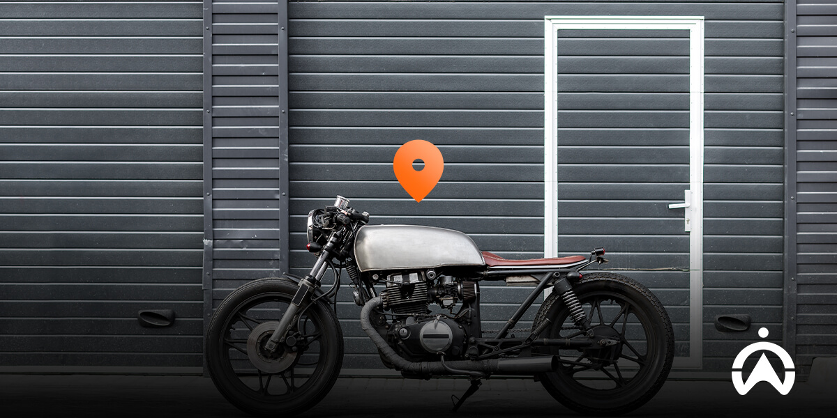 A vintage motorcycle parked beside a gray wall with a white door, featuring a location pin icon above it.
