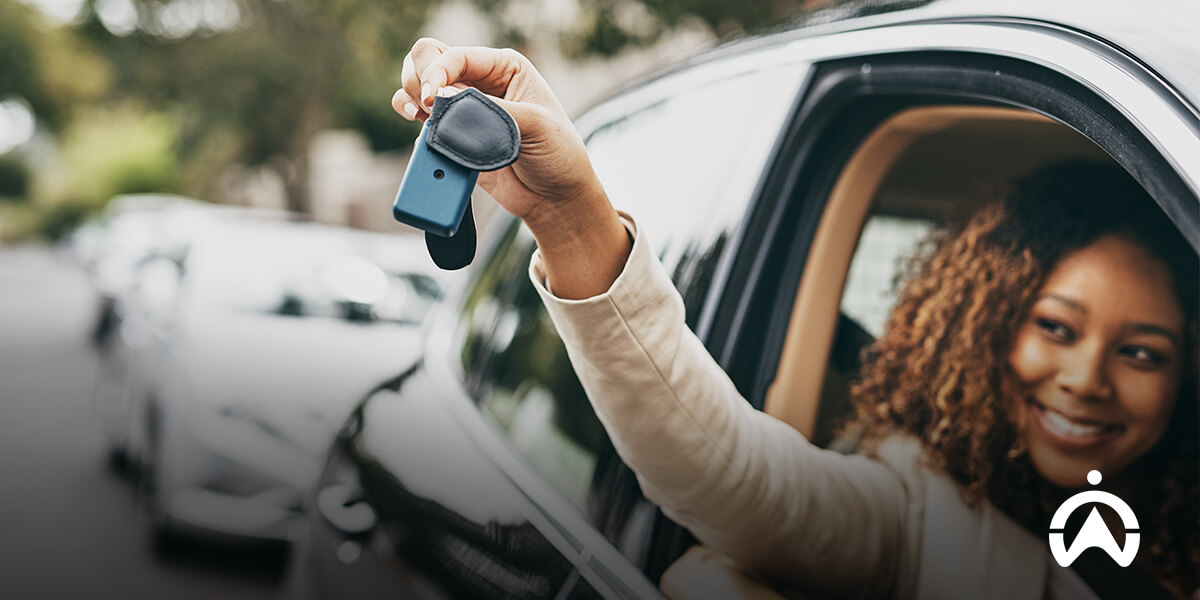 Hand holding car keys outside a vehicle displaying personal car tracking device.