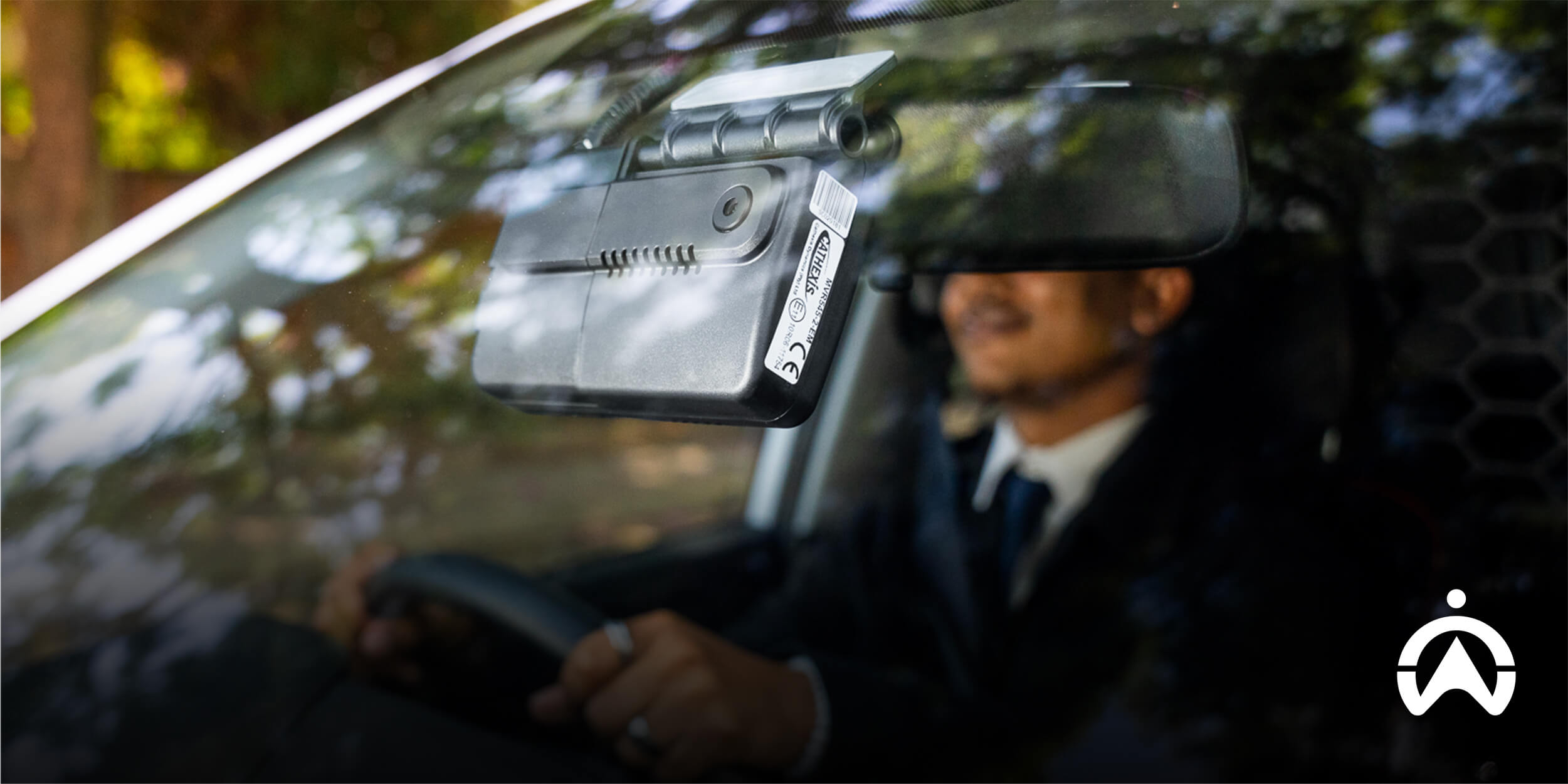A driver in a suit holds the steering wheel, with camera with GPS tracker mounted on the windshield capturing the view ahead.