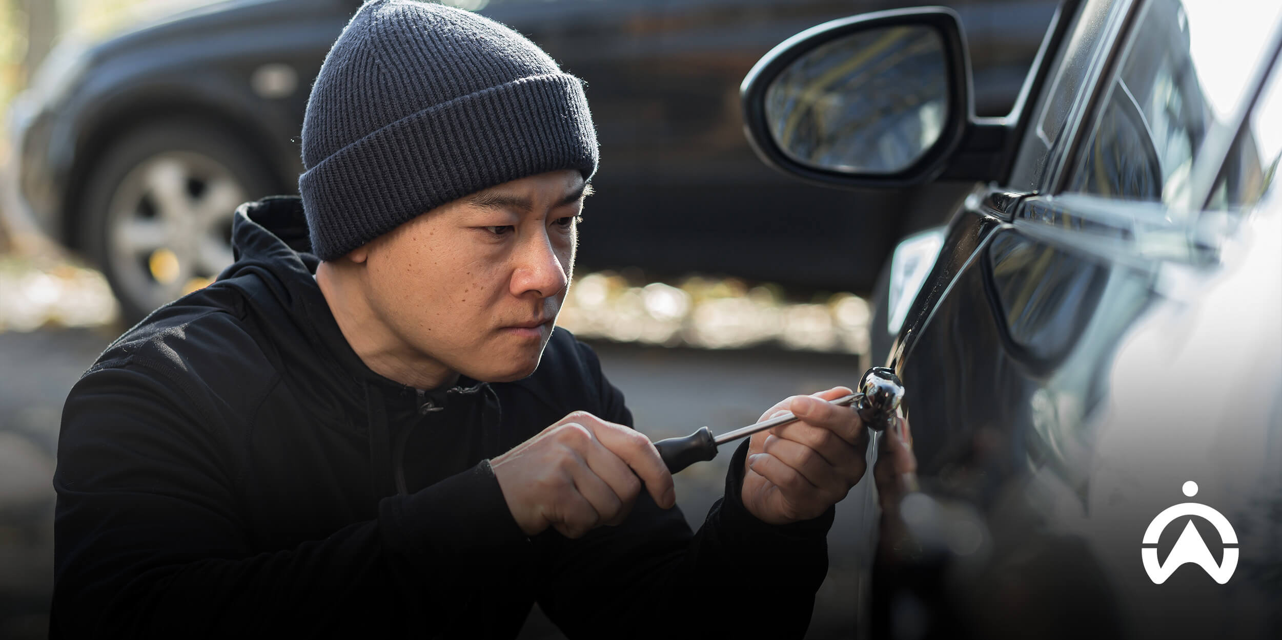 Person tampering with vehicle, highlighting need for an insurance-approved vehicle tracker for theft protection.