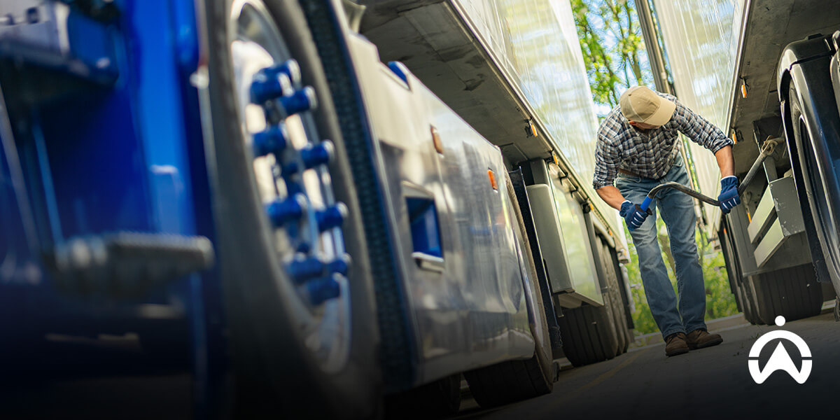 Mechanic inspecting truck undercarriage as part of fleet safety certification requirements and compliance checks.