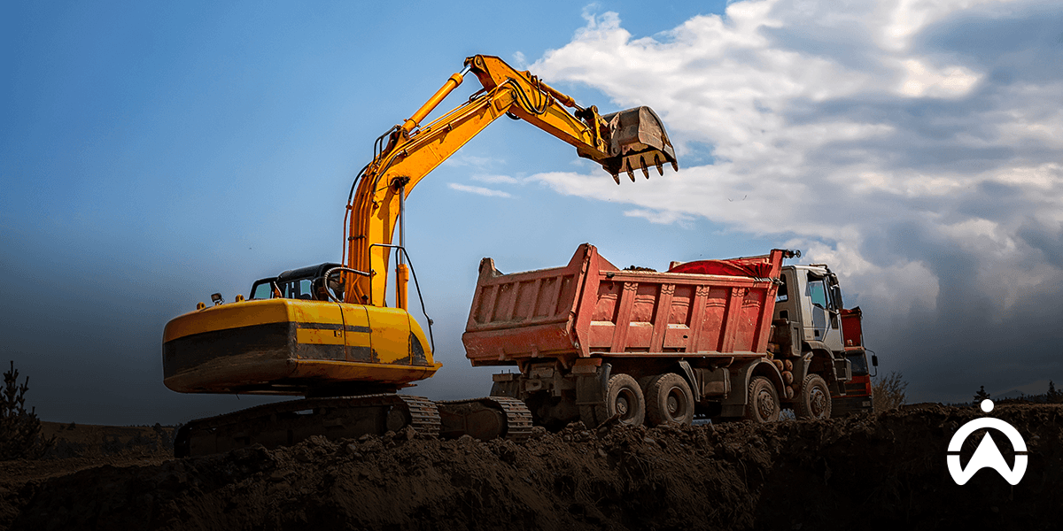 Yellow excavator loading soil into a red dump truck at a construction site under a partly cloudy sky.