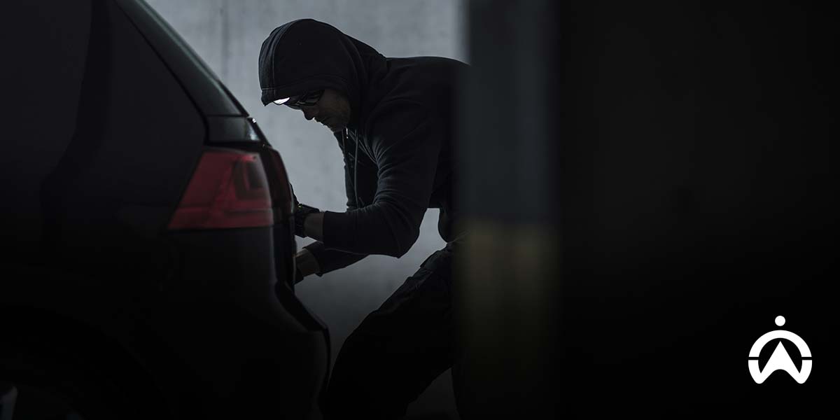 Person attempting car break-in in parking area, highlighting risks of remote jamming and vehicle security threats.