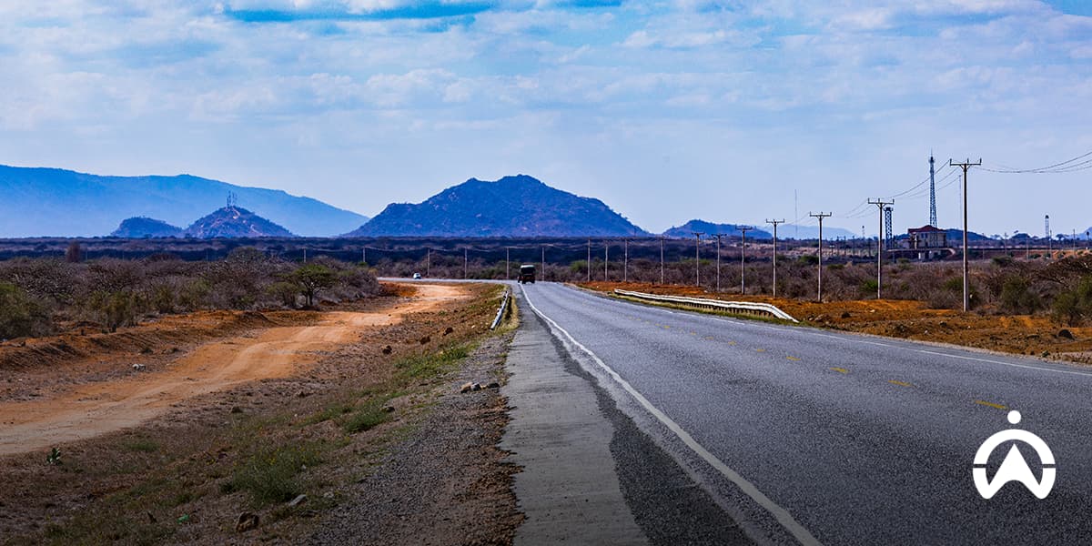 Long rural road through mountainous terrain with power lines, reflecting the current state of South African roads.