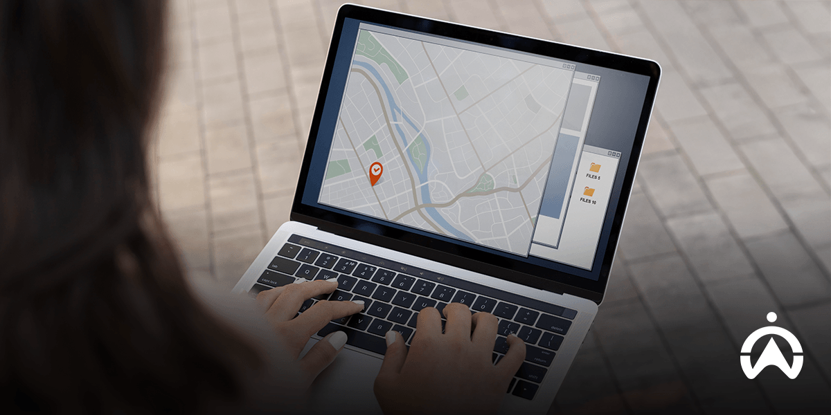 A person using a laptop to monitor GPS tracking software with a location pin and data folders visible on the screen.