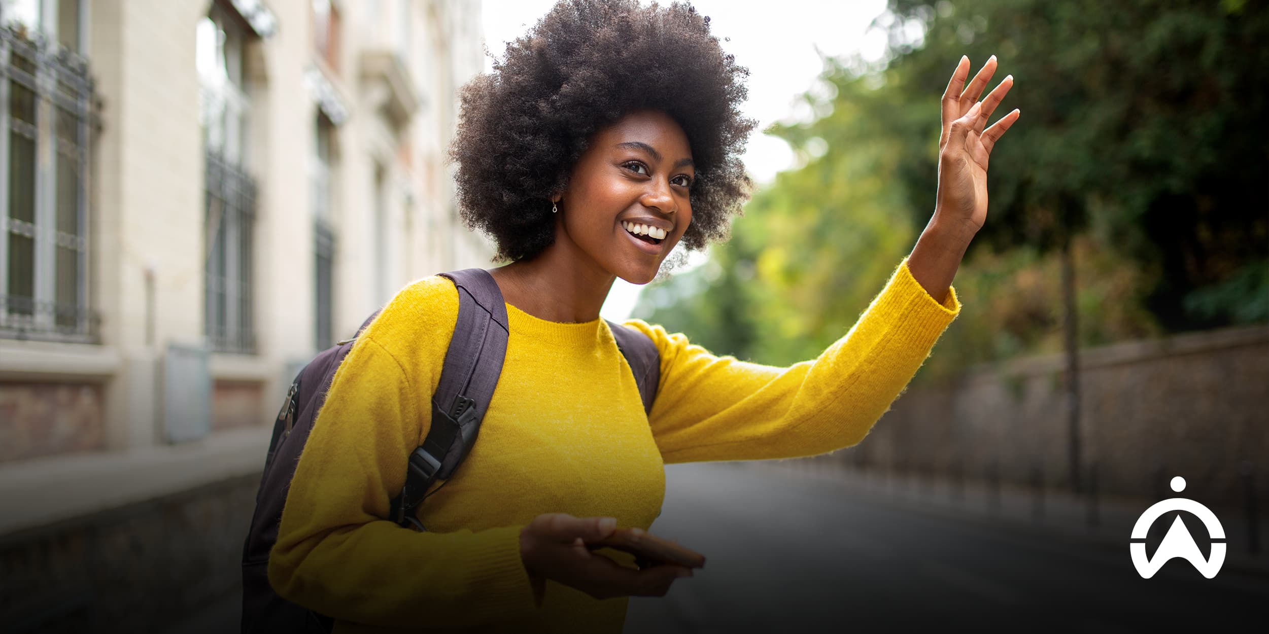 Joyful woman with curly hair waving while holding her phone on a sunny street, illustrating customer demand and opportunities when learning how to start an e-hailing business