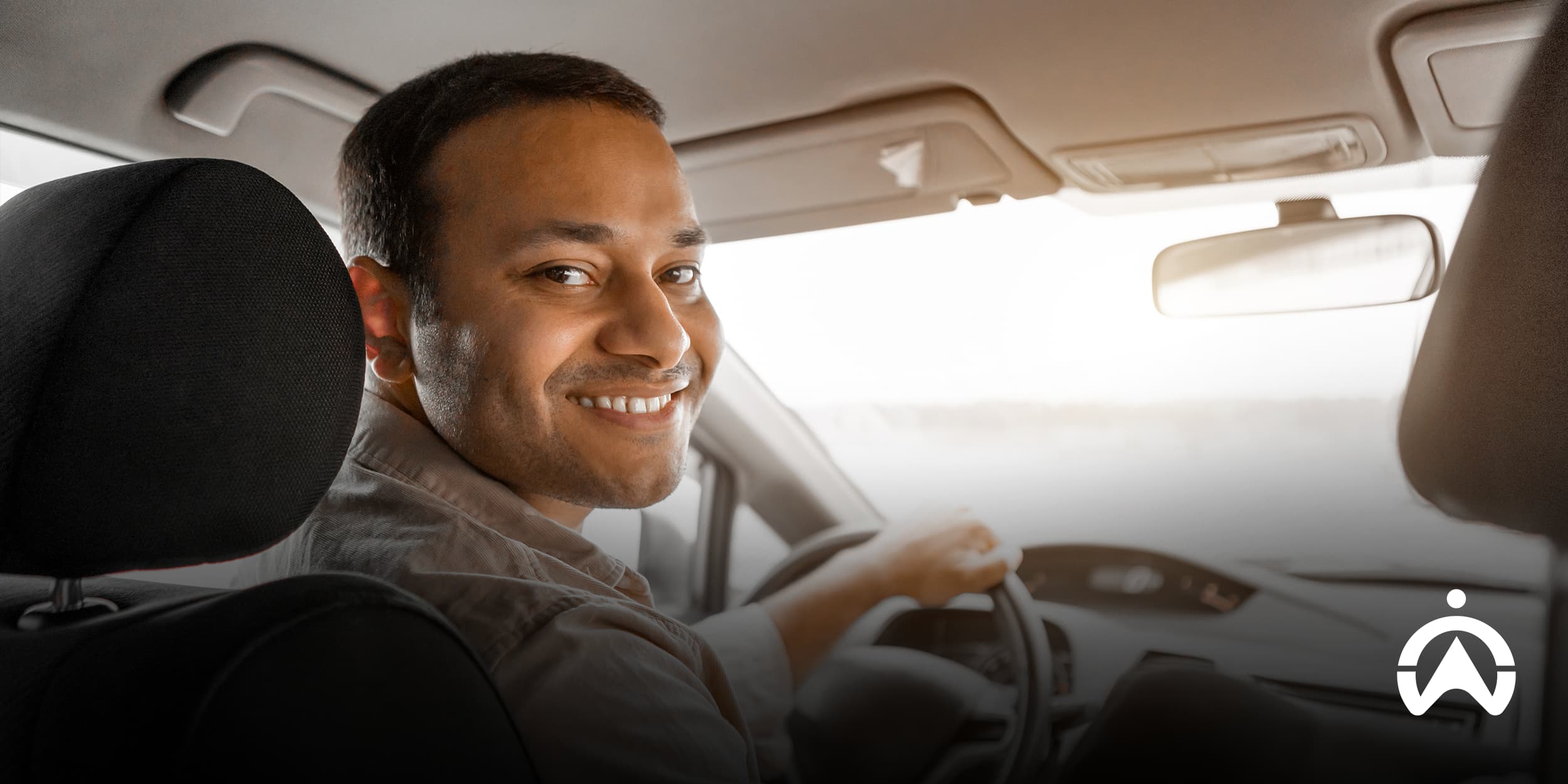 Smiling man driving a car and looking back over his shoulder, representing how to start an e-hailing business with a positive and confident driver experience in a bright, relaxed interior