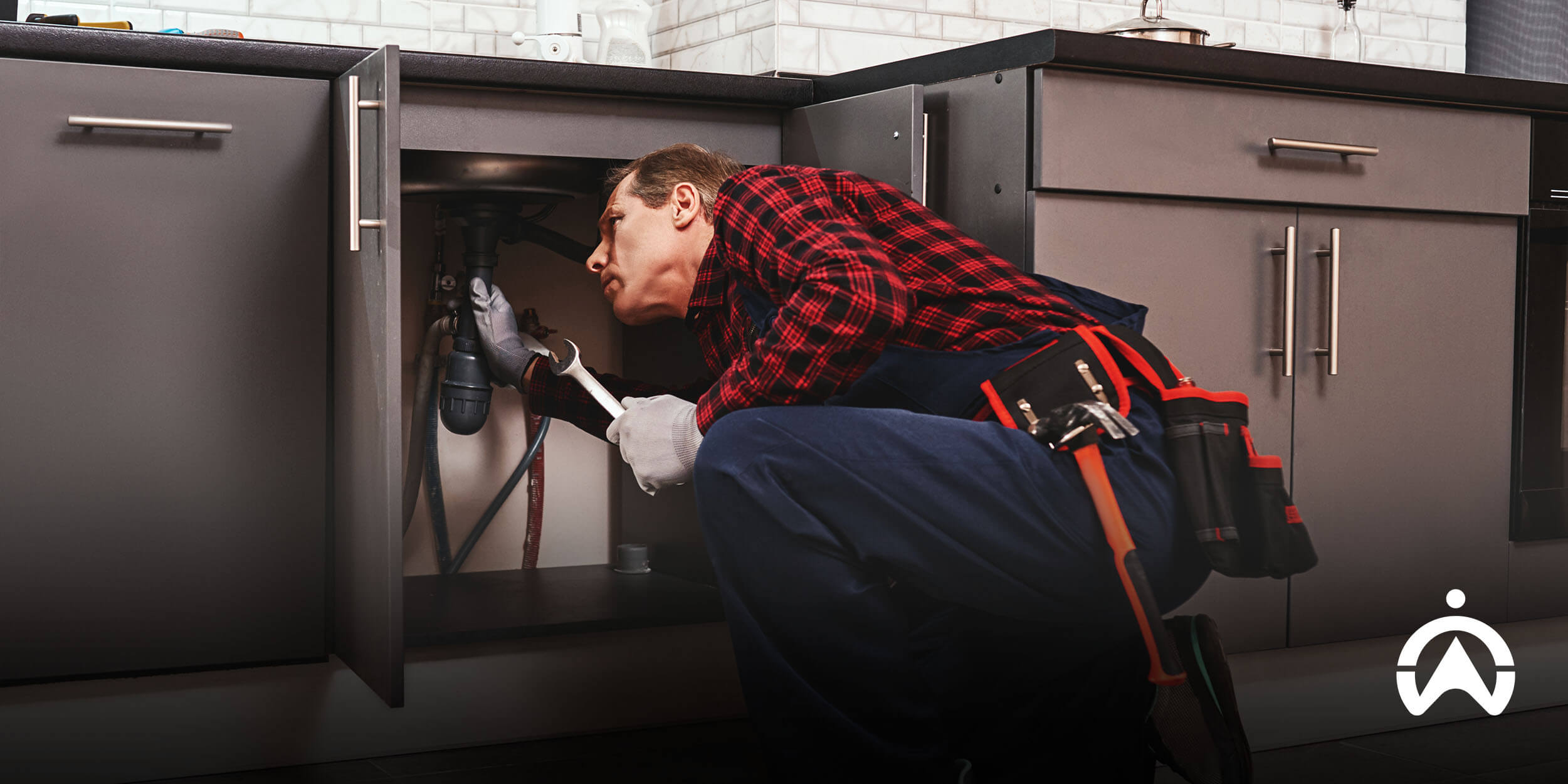Plumber fixing pipes under a kitchen sink with tools, illustrating how field service management software for small business supports job tracking and maintenance work