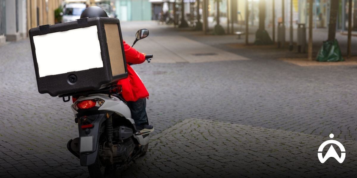 Delivery rider on a scooter with insulated box on a cobblestone street, illustrating bike sharing software for managing urban delivery fleets