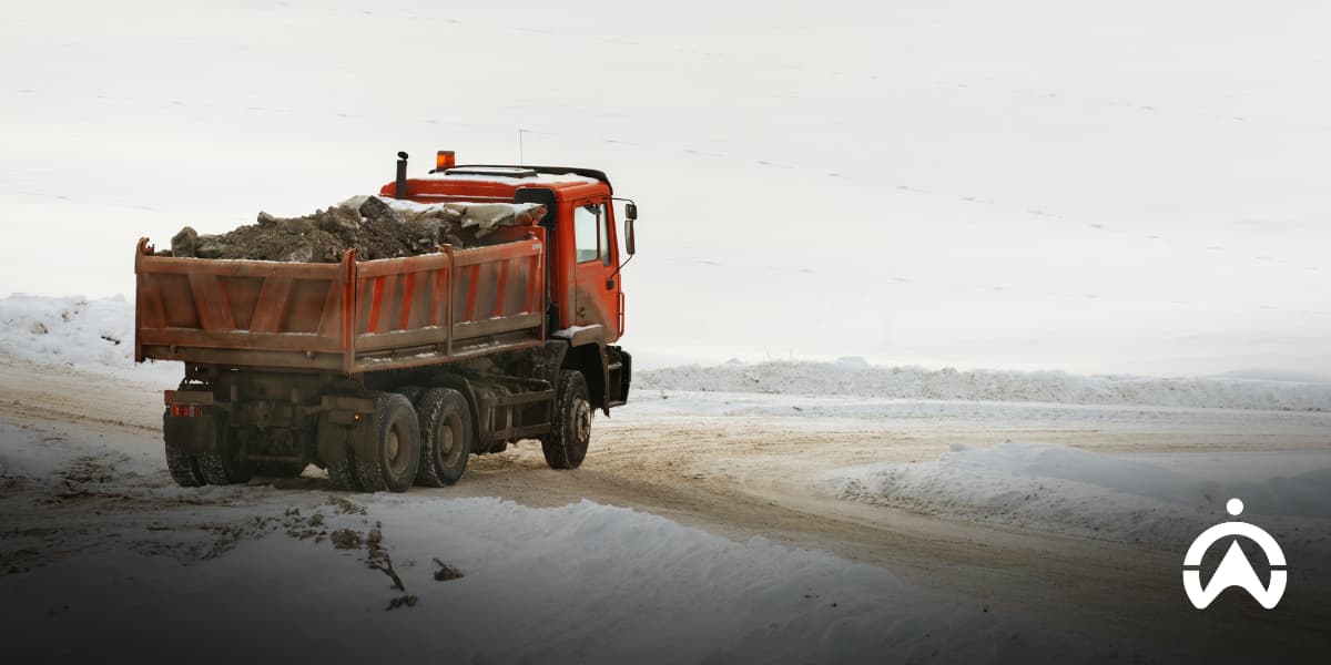 Orange dump truck driving on a snowy road, illustrating cold weather maintenance tips for your trucks during winter transport operations