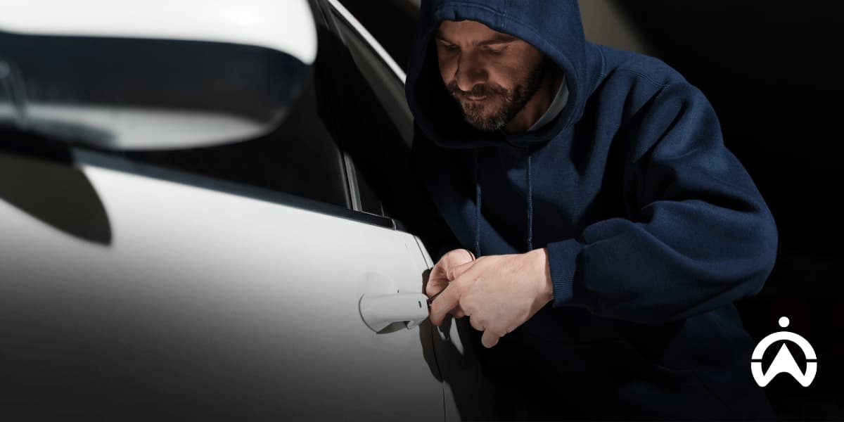 A person in a dark hoodie using a tool to break into a white car, illustrating what fails to prevent car and vehicle theft.