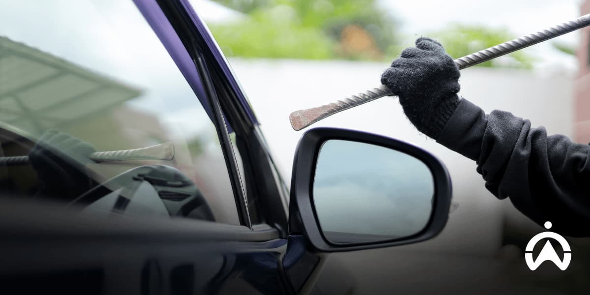 A gloved hand holding a metal crowbar near a car window, illustrating a break-in attempt for an article on how to prevent car and vehicle theft.