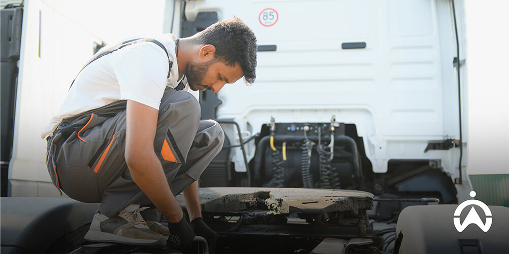 Mechanic inspecting a truck's fifth wheel coupling during cold chain system maintenance