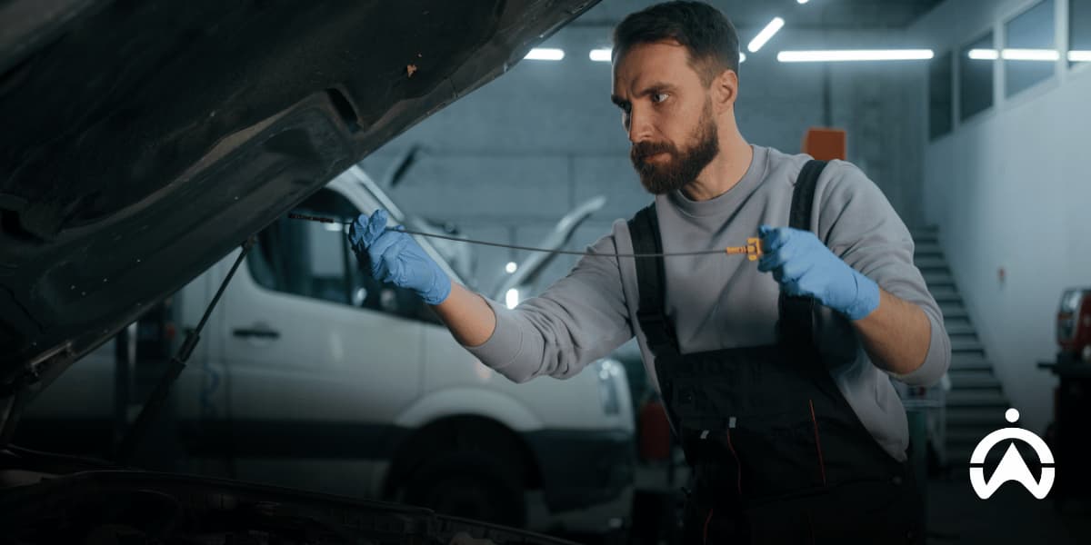 Mechanic checking engine oil with a dipstick as part of routine fleet maintenance and vehicle servicing.