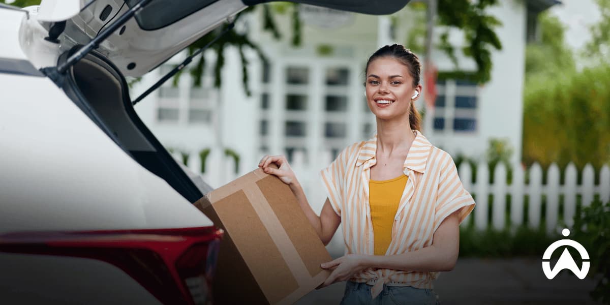 Woman loading a cardboard box into her car outside a house, highlighting car safety considerations when moving to South Africa.