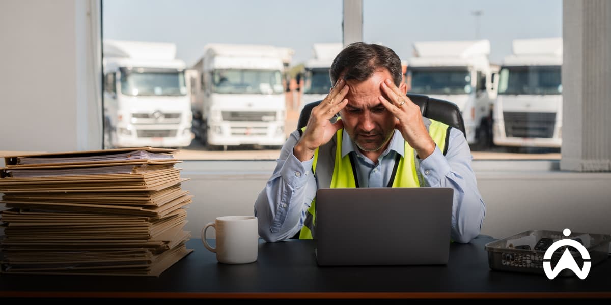 Stressed truck dispatcher reviewing paperwork at a laptop, illustrating fleet management survey findings on operational challenges and workload.