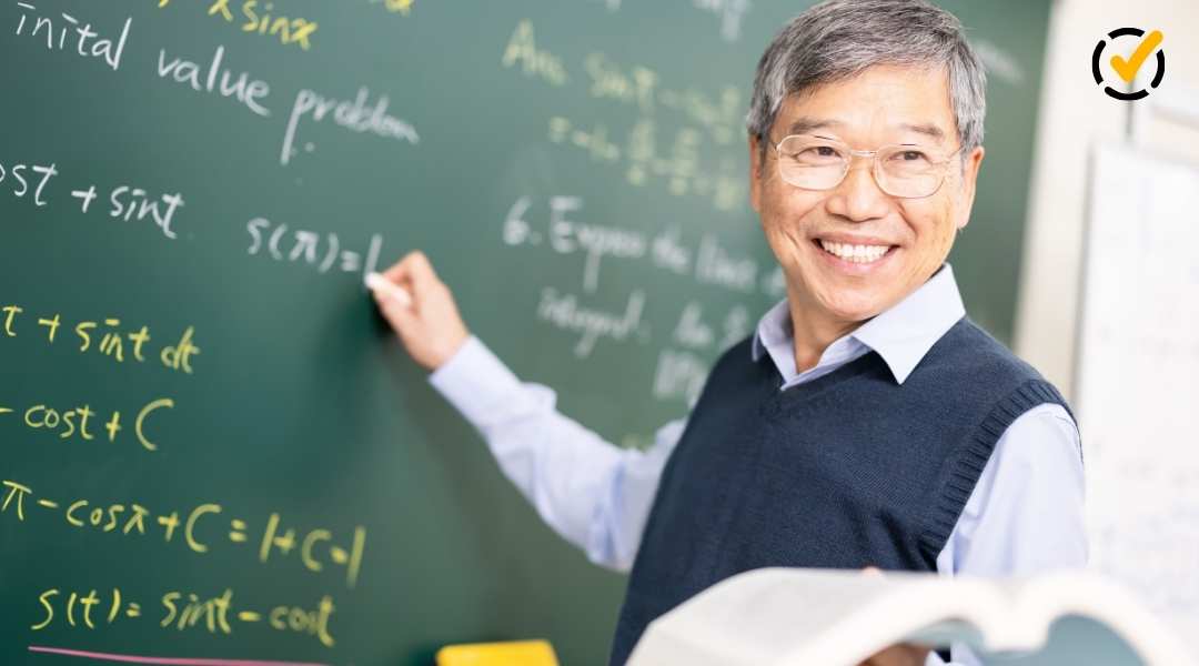 "A smiling male math teacher wearing glasses holds an open book and points to a green chalkboard covered in handwritten mathematical equations. The Formative by Newsela logo is in the top right corner."