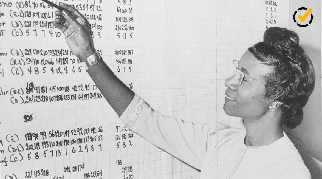 "A black and white image of an African American woman wearing glasses and with her hair in an updo, smiling and pointing at a large document filled with columns of handwritten numbers. The Formative by Newsela logo is in the top right corner."