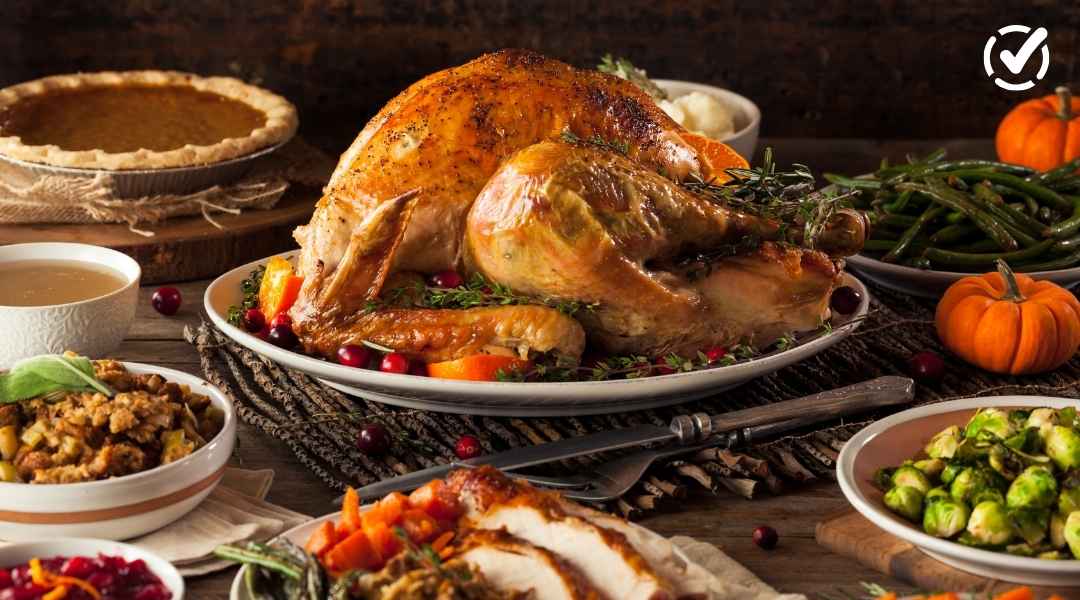 "A roasted turkey garnished with herbs and cranberries is centered on a platter, surrounded by various Thanksgiving side dishes like pumpkin pie, green beans, and brussels sprouts. Two small decorative pumpkins are also visible. The Formative by Newsela lo