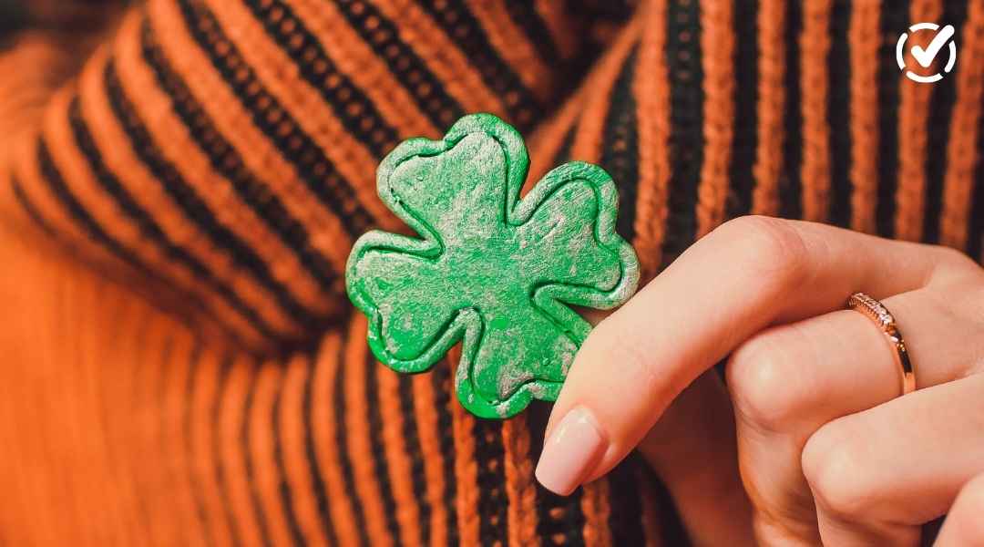 "A hand with manicured nails touches a green shamrock pin attached to an orange and black striped sweater. The Formative by Newsela logo is in the top right corner."