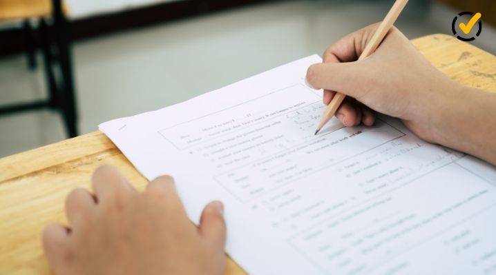 Close-up of a K-12 student using a pencil to complete a paper worksheet in a classroom, representing formative and summative assessments.
