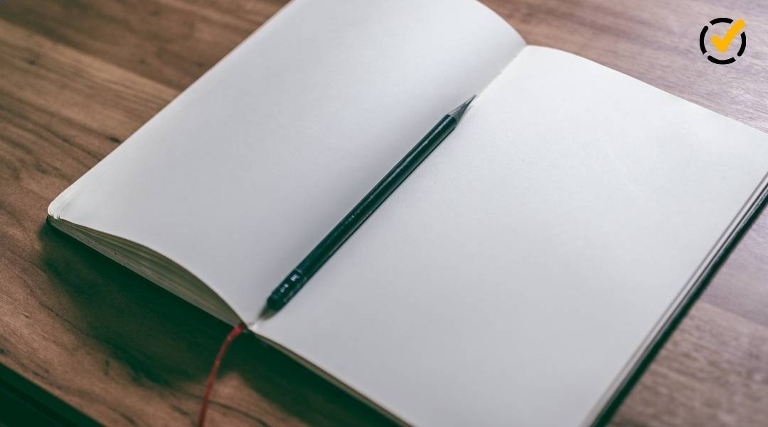 A close-up, overhead view of an open notebook with blank pages and a dark pencil resting in the center crease.