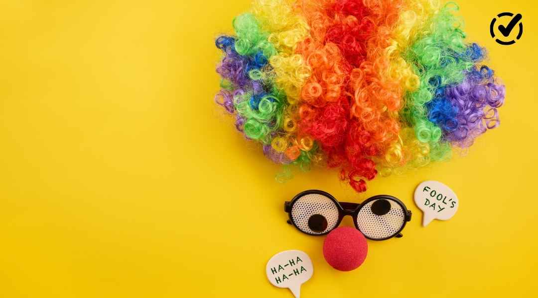 A playful April Fools' Day themed image on a yellow background featuring a rainbow clown wig, novelty googly-eye glasses with a red nose, and speech bubbles saying "HA-HA" and "FOOL'S DAY."