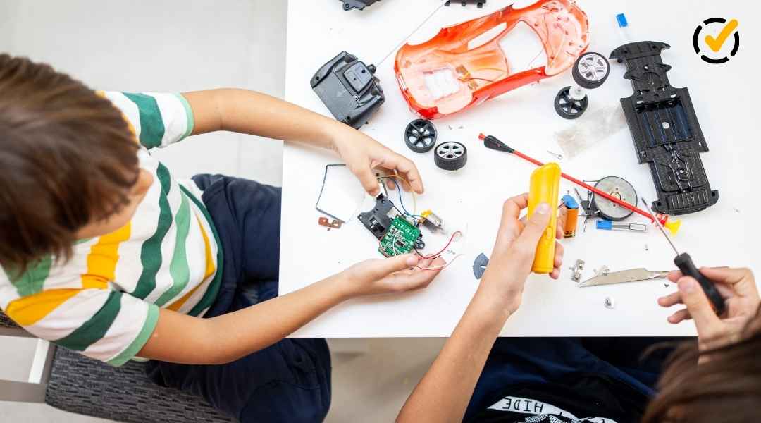 Overhead view of two children collaborating on a hands-on robotics project at a white table covered in wires, circuit boards, and plastic robot car parts. A Formative by Newsela logo is in the top right corner.