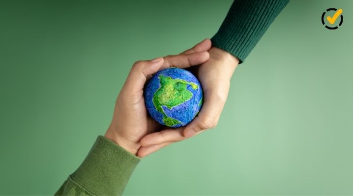 Close-up of two hands holding a small, handmade globe of Earth. The background is a soft green, and the Formative logo appears as a small yellow checkmark icon in the top right corner.