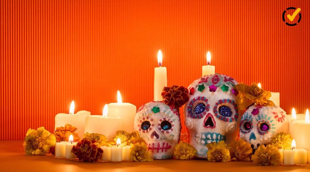 Three colorful decorative skulls surrounded by lit candles and marigolds in a Día de los Muertos display.