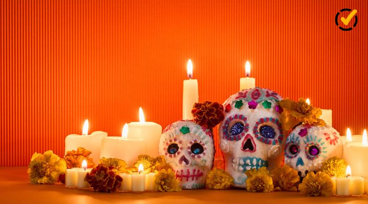 Three colorful decorative skulls surrounded by lit candles and marigolds in a Día de los Muertos display.