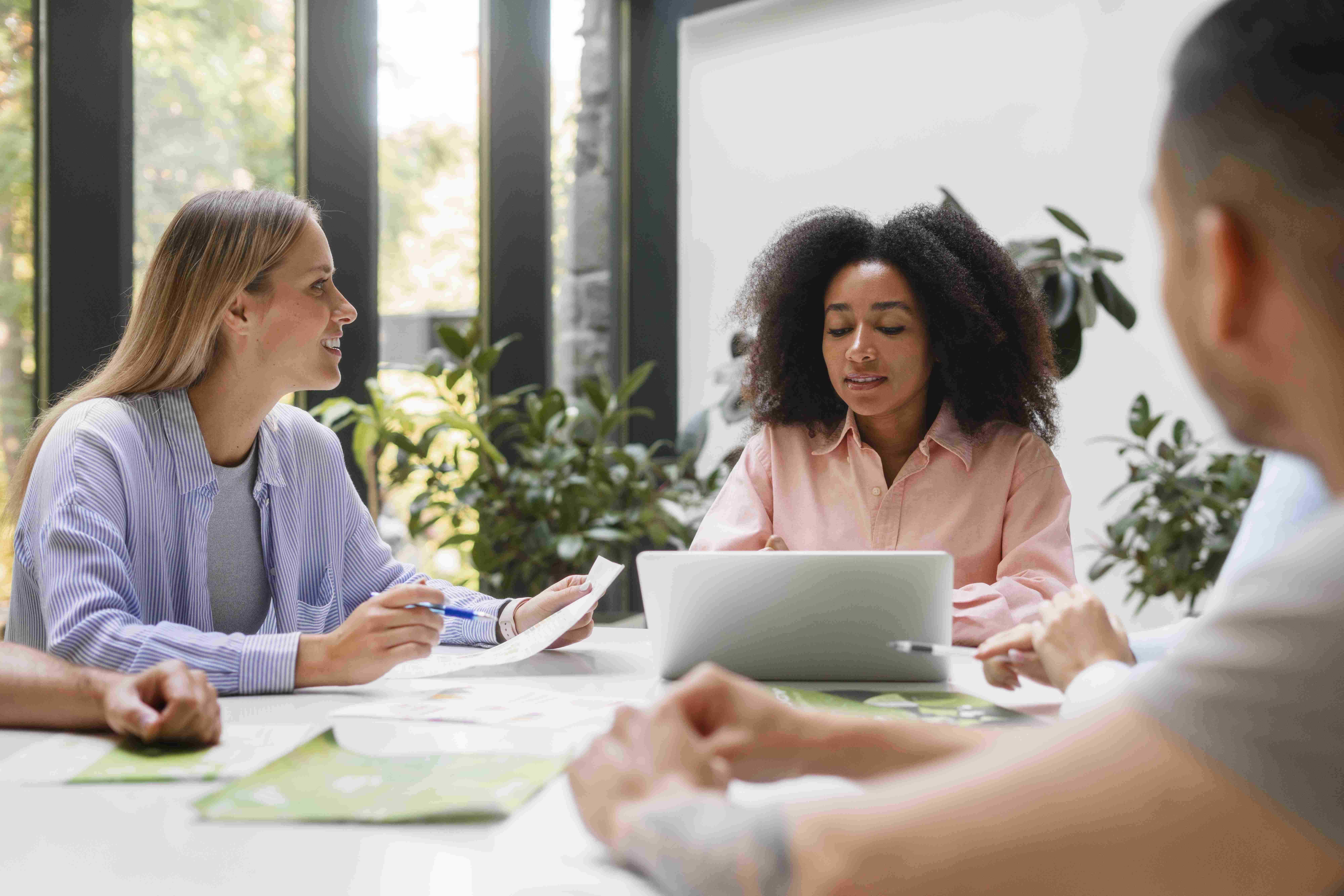 Duas mulheres reunidas em uma mesa de trabalho, em frente ao notebook.