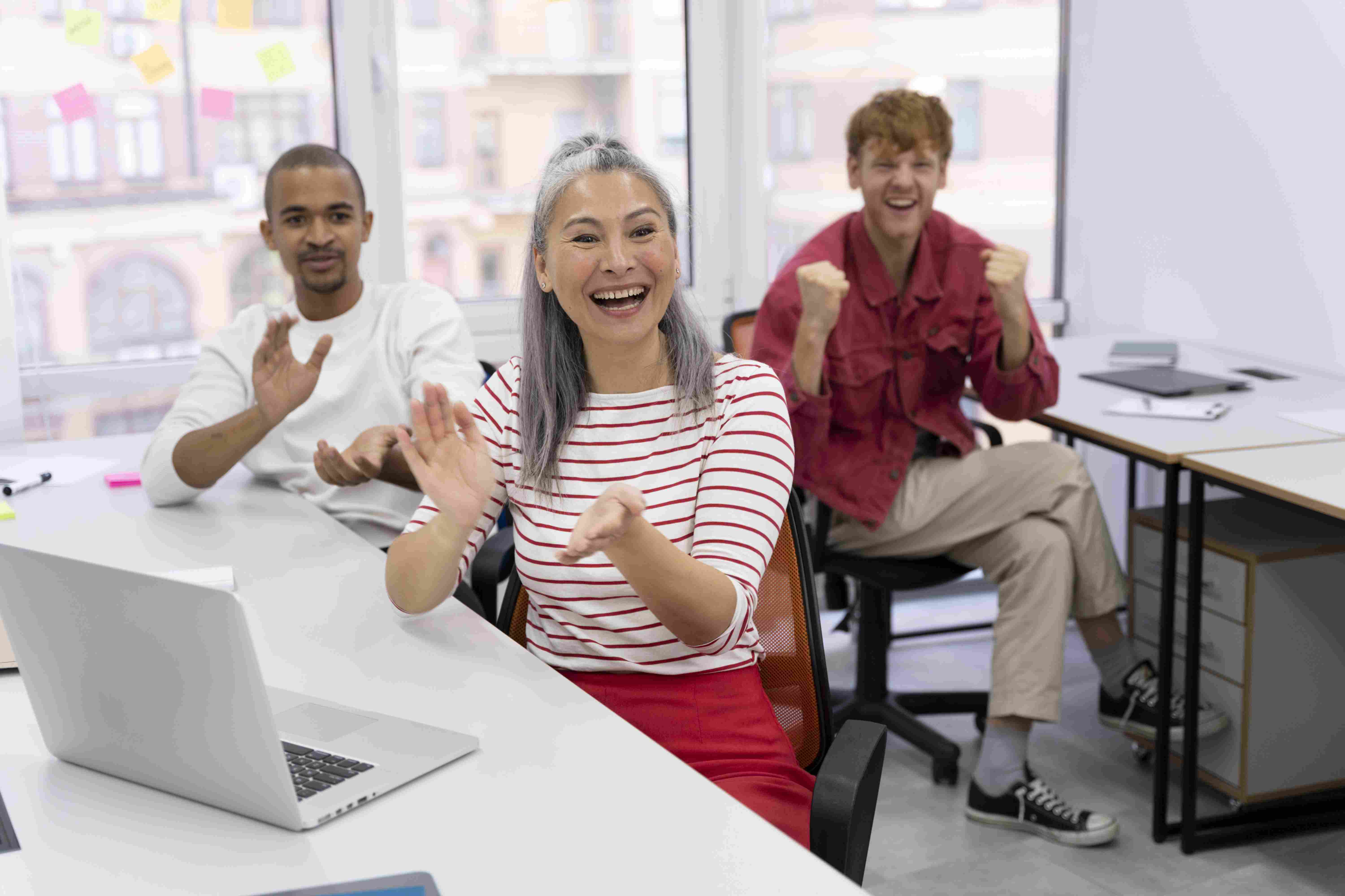 Mulher asiática e dois homens comemorando conquista no ambiente de trabalho.