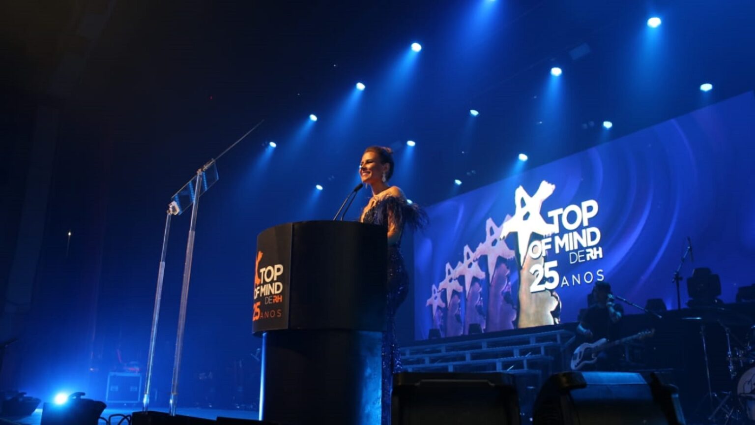 Mulher em palanque, apresentando o evento Top of Mind de RH.