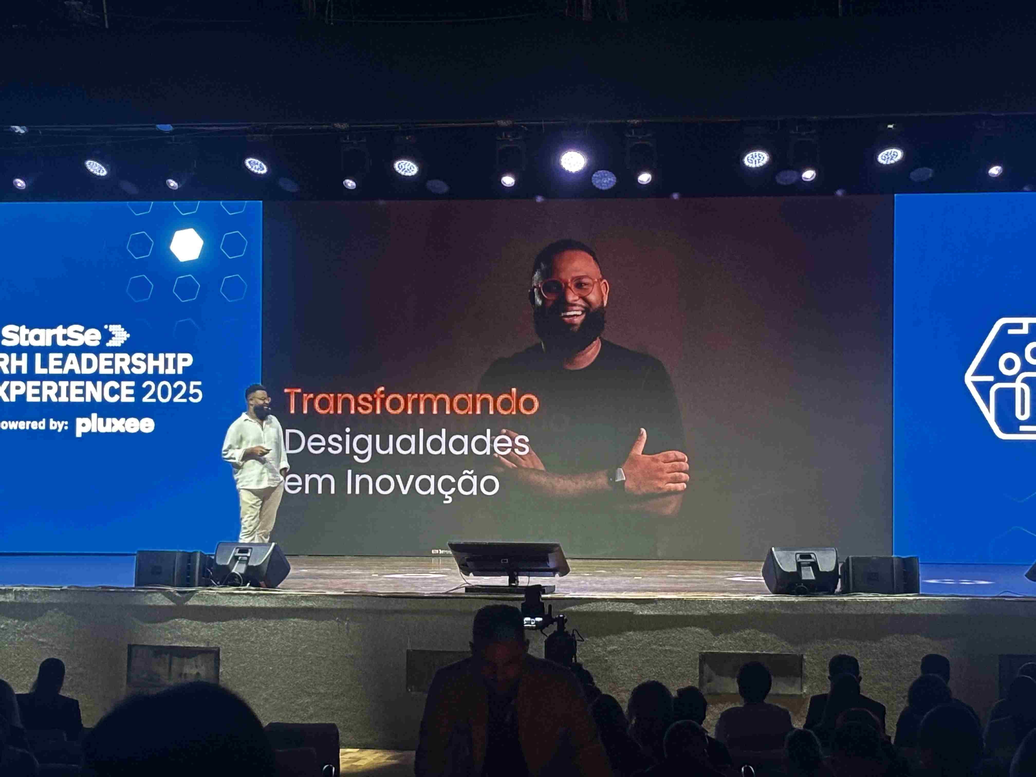 Palestrante no RH Leadership Xperience, com telão escrito "transformando desigualdade em inovação" ao fundo.