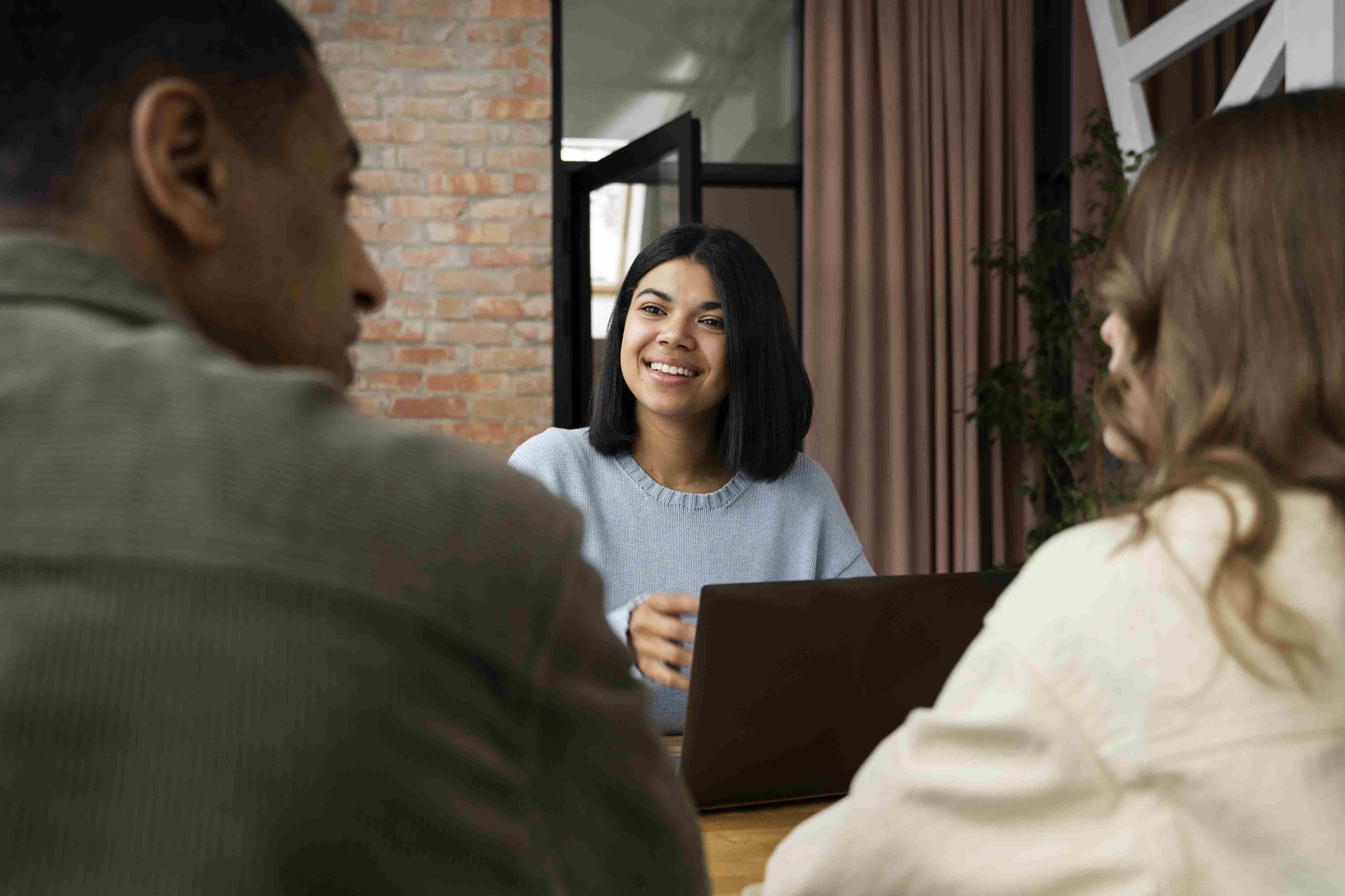 Duas mulheres e um homem reunidos ao redor de uma mesa, conversando durante o trabalho.