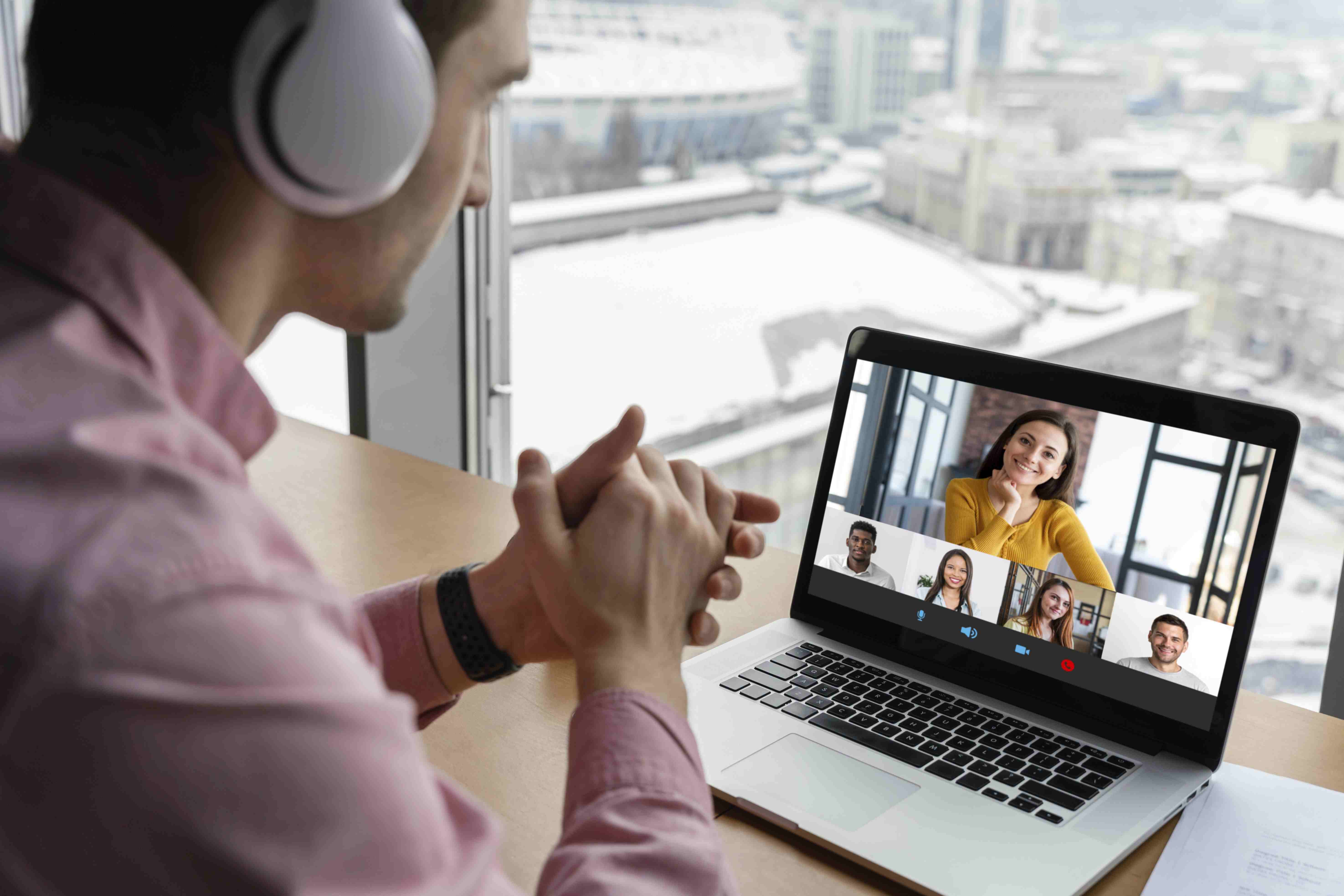 Homem de camisa rosa, com fones de ouvido, fazendo reunião online com outras cinco pessoas.