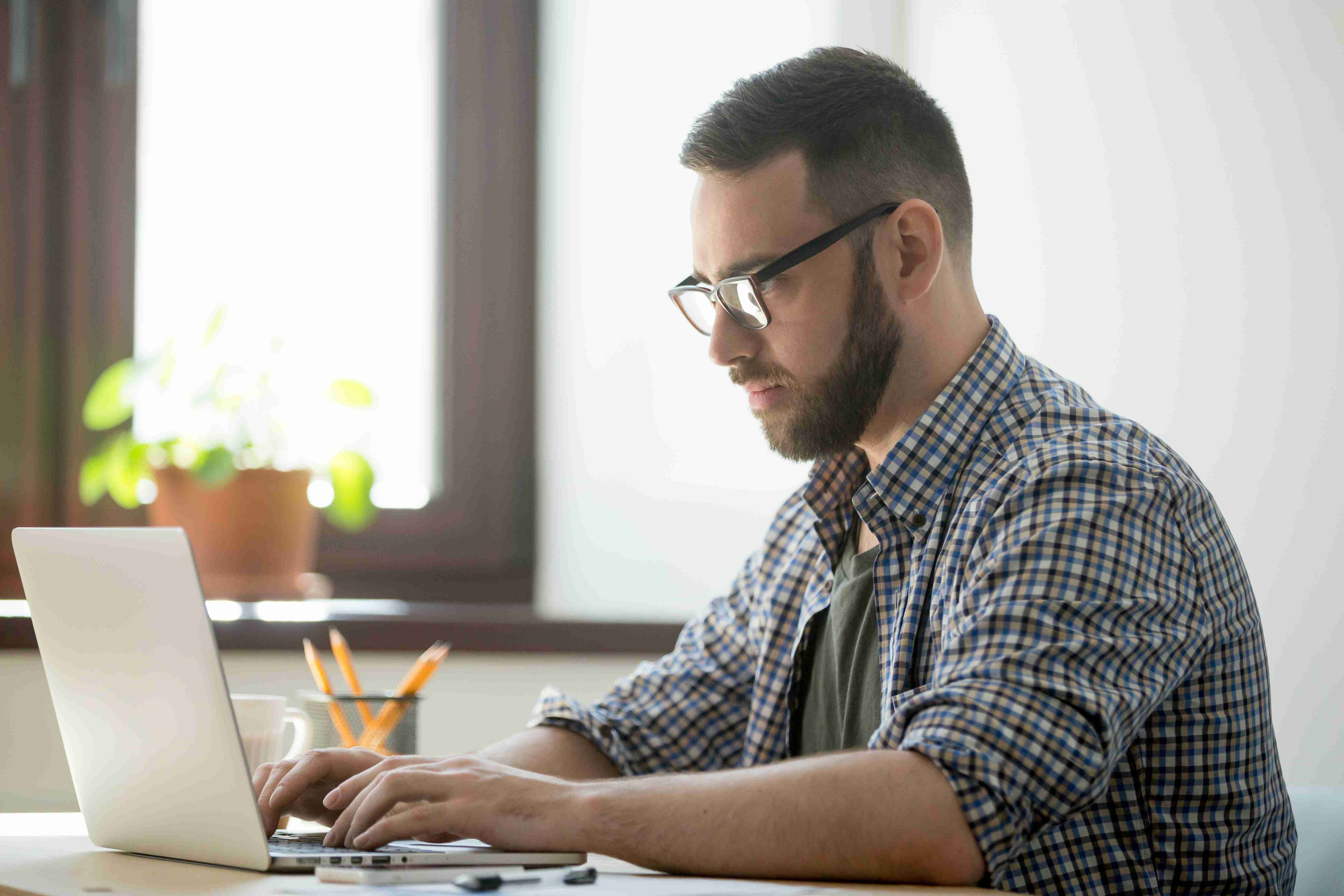 Homem sentado à mesa, em um notebook, digitando em um patient management system.