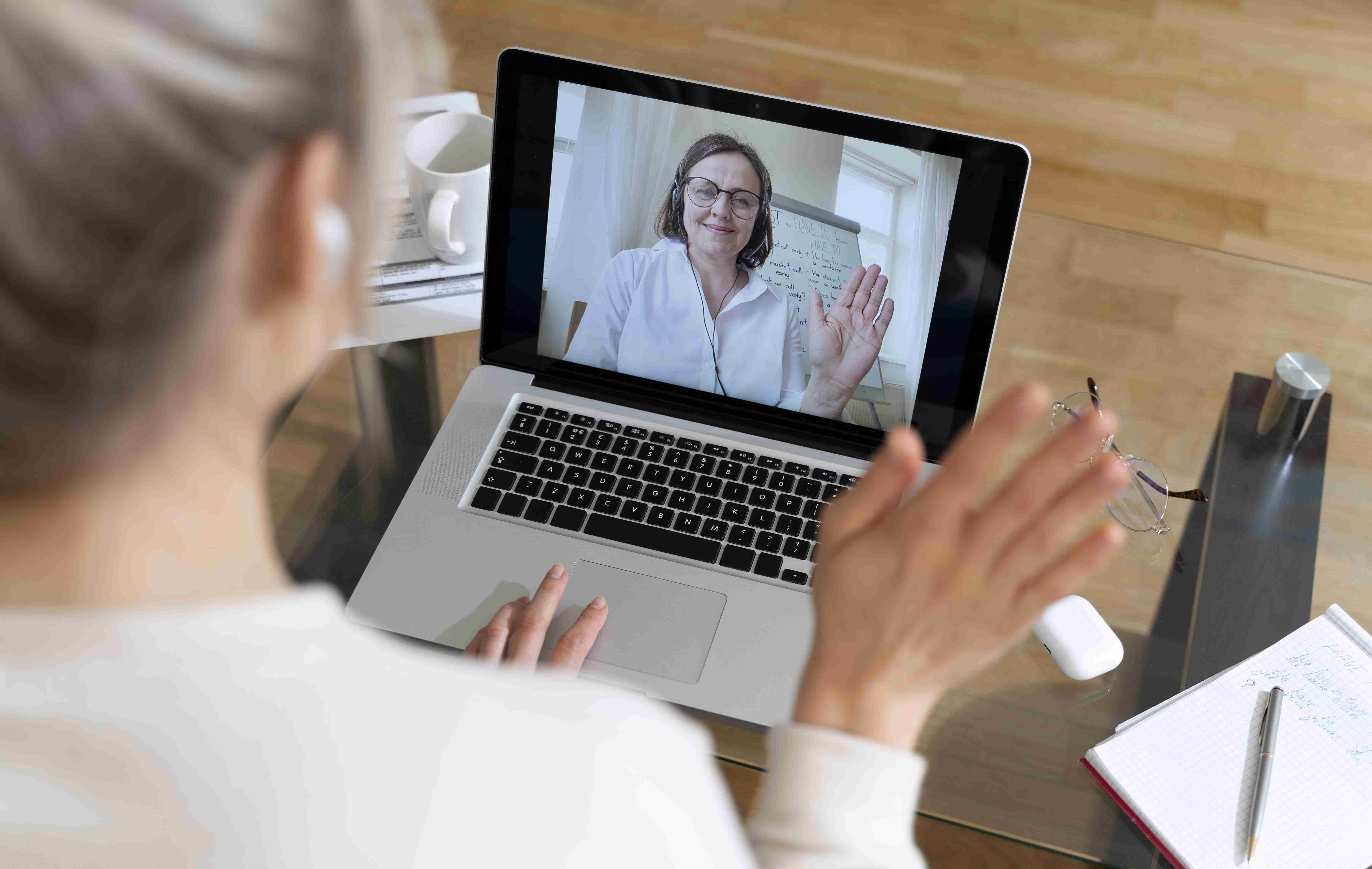 Mulher realizando teleconsulta e acenando para profissional de saúde, que também acena.