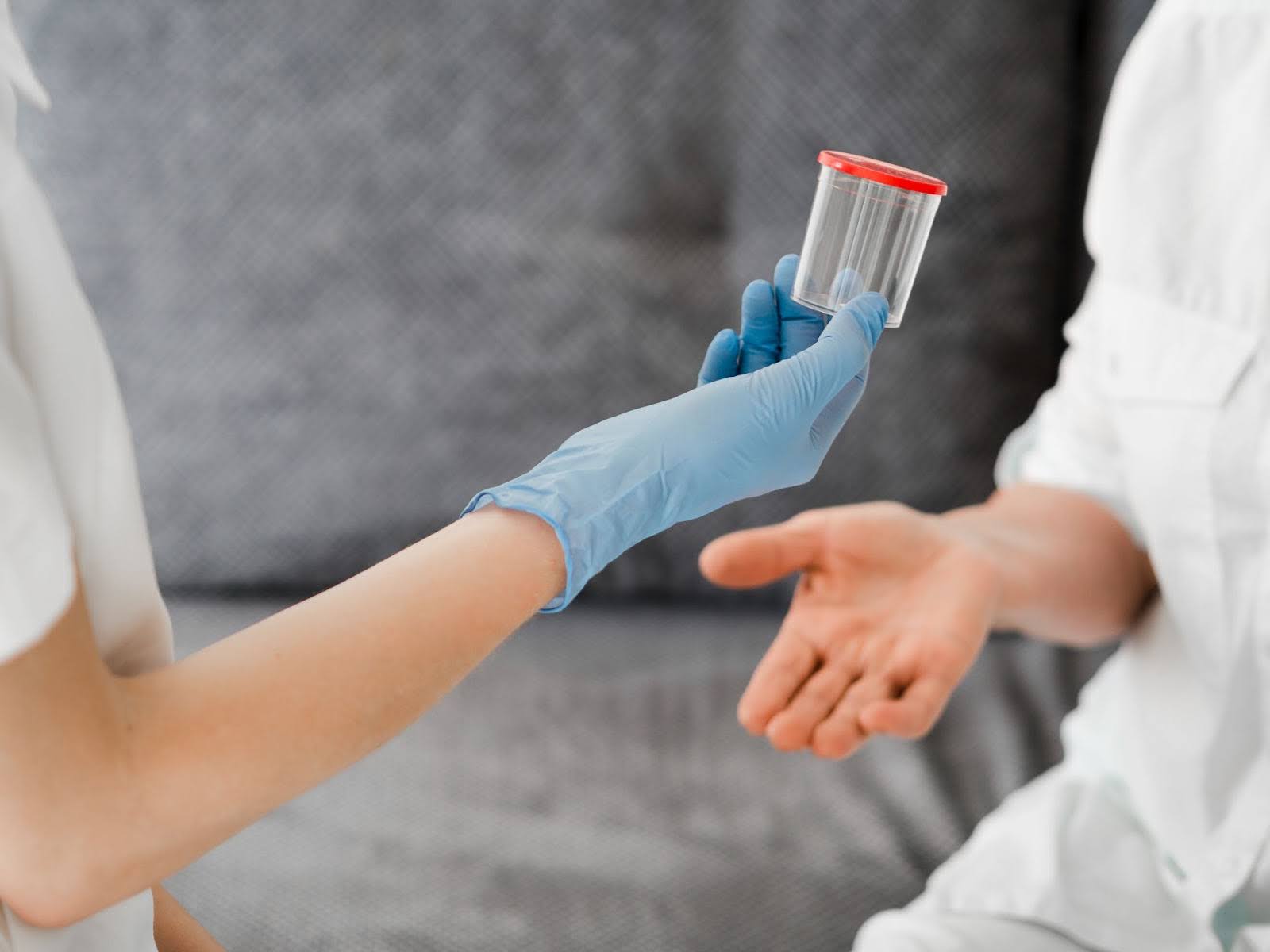 Enfermeira entregando pote de plástico para realização do exame de urina, comum no check-up médico.