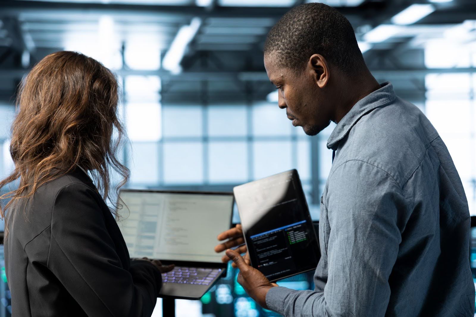 Homem e mulher, segurando notebook e tablet, respectivamente, conversando sobre dados.