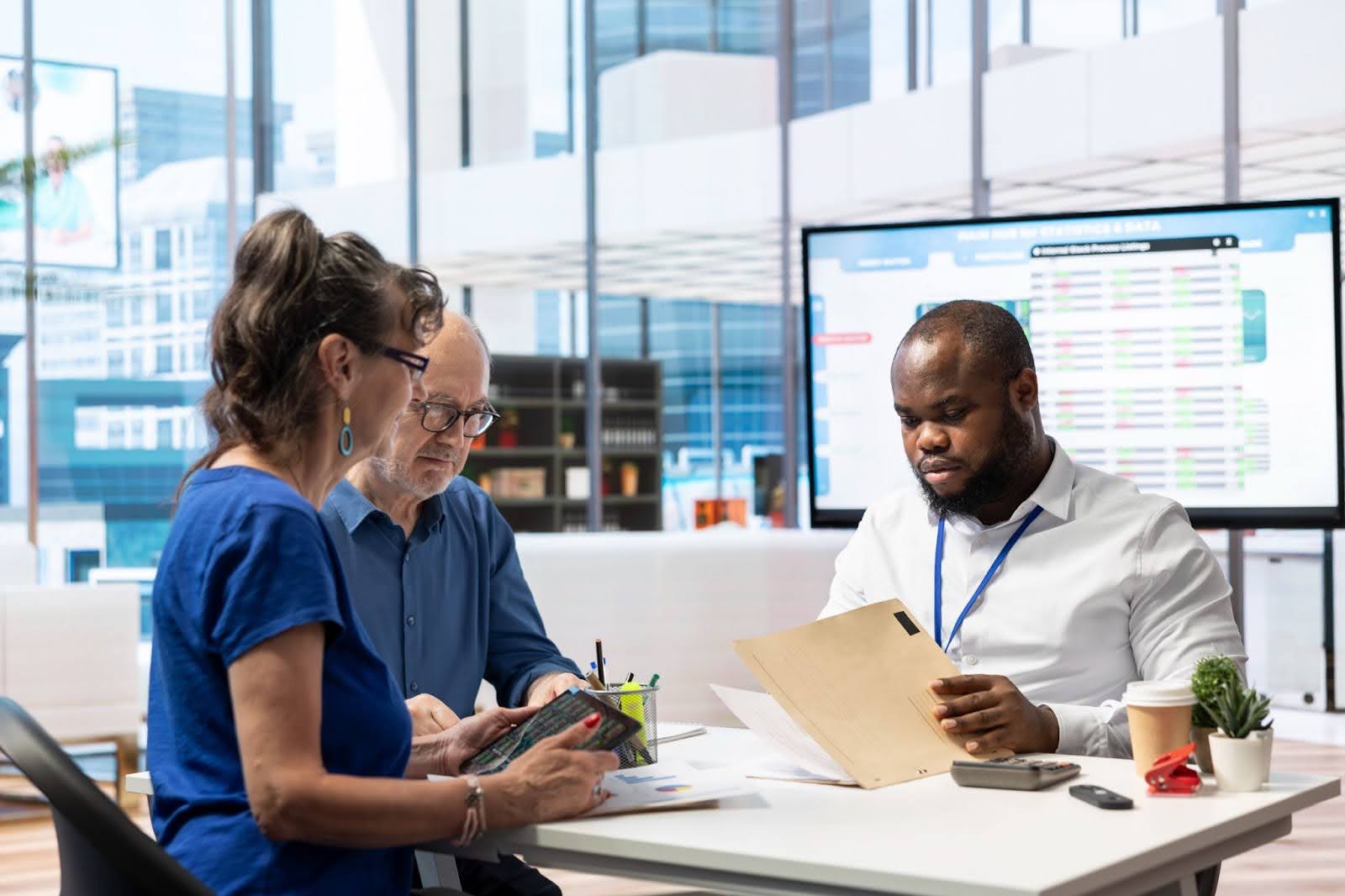 Três profissionais de saúde reunidos ao redor de uma mesa, analisando dados em papeis e em um tablet.