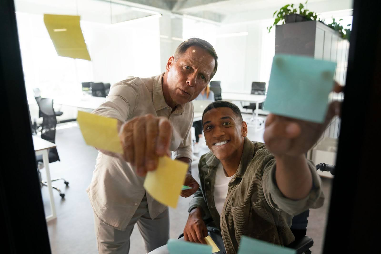 Dois homens no local de trabalho, colando post its em uma parede de vidro.