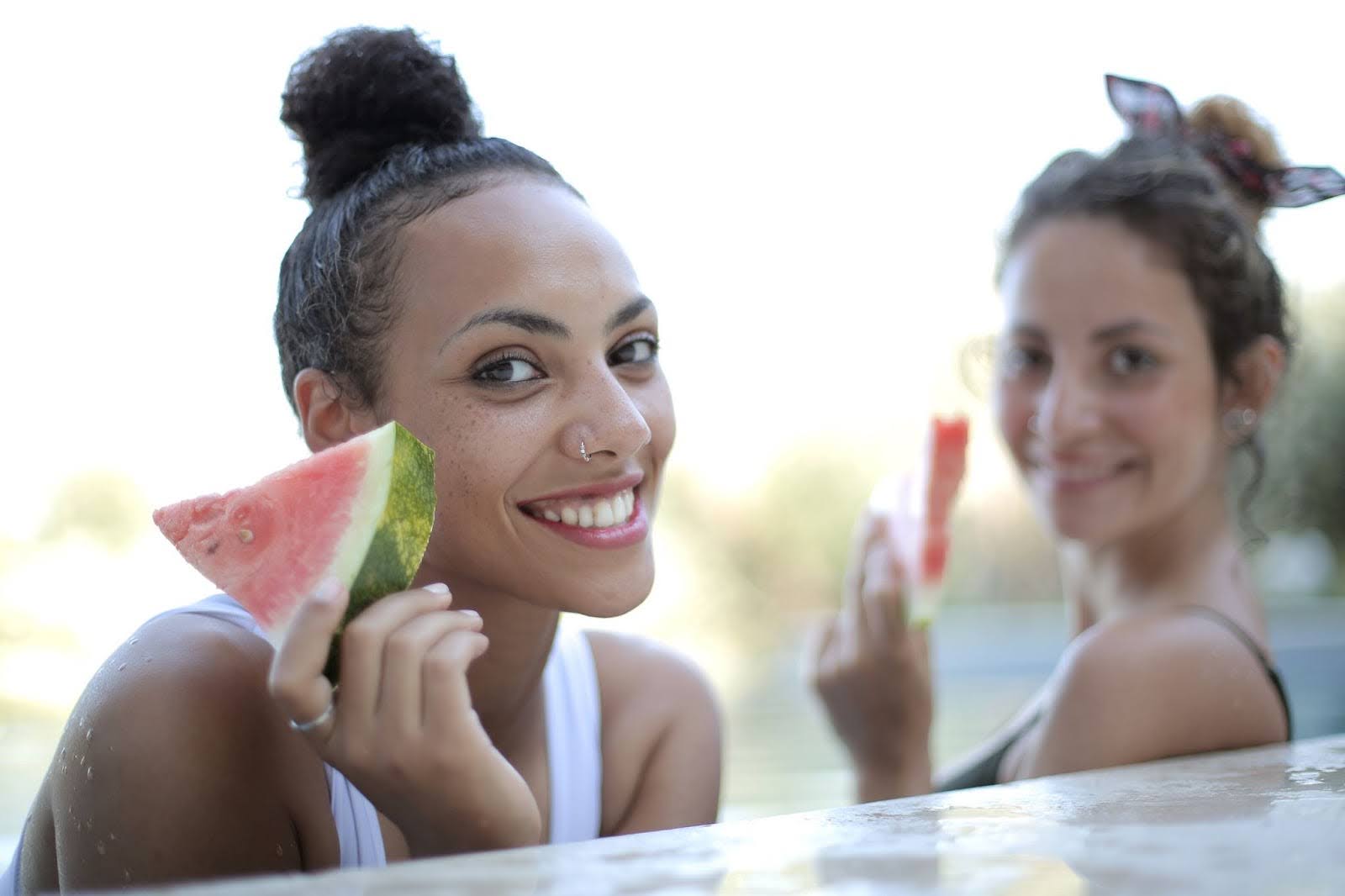 Duas mulheres, sorrindo, enquanto comem melancia.