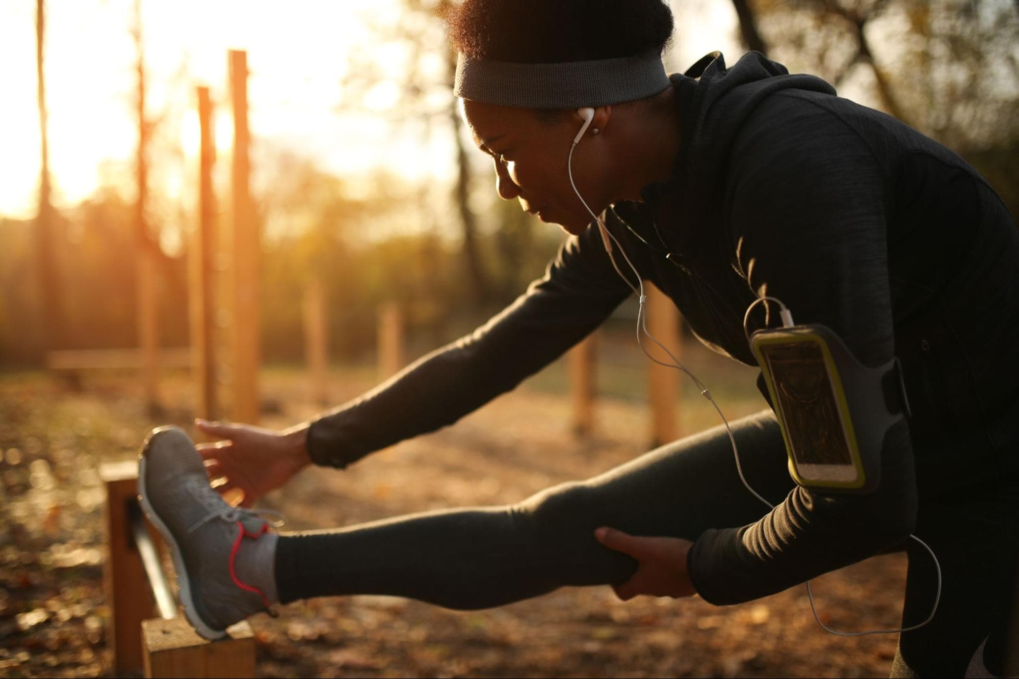 Mulher se alogando em um parque, com roupas de praticar exercício.