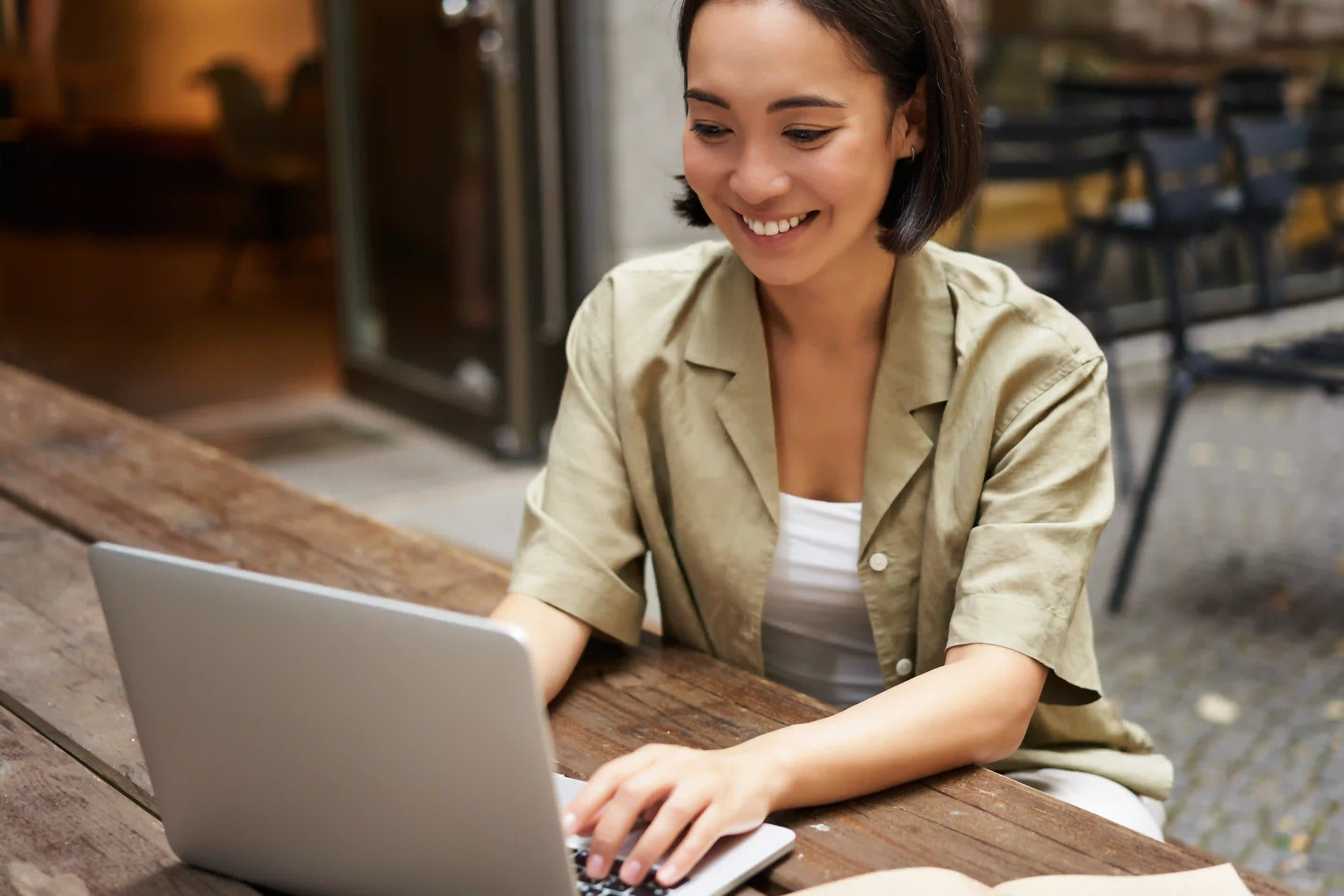 Mulher sorrindo enquanto digita em um notebook, sentada ao ar livre.