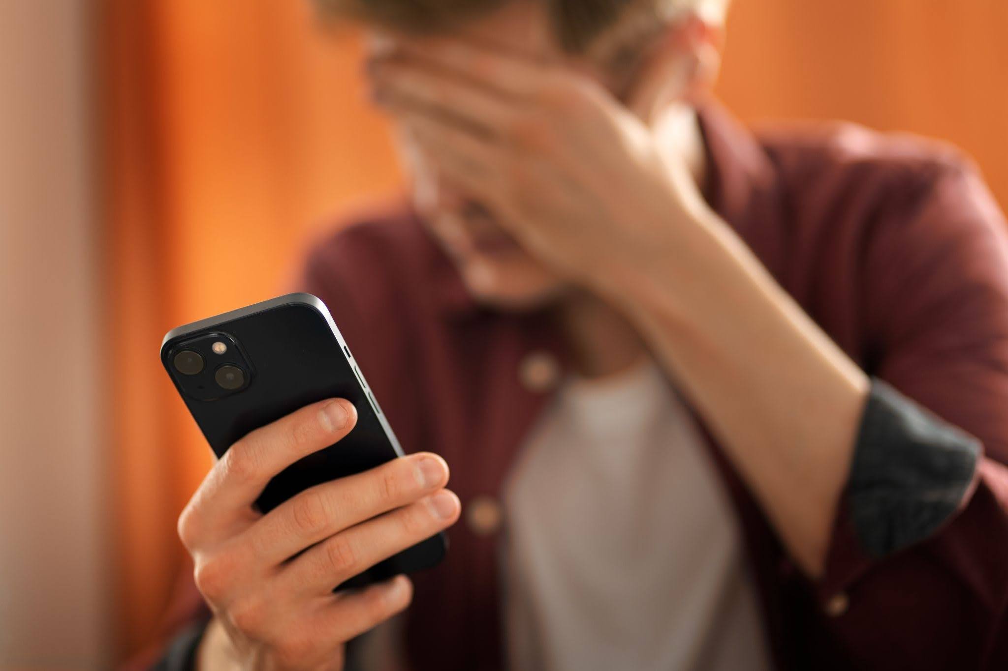 Homem segurando celular e tampando os olhos para não olhar para a tela.