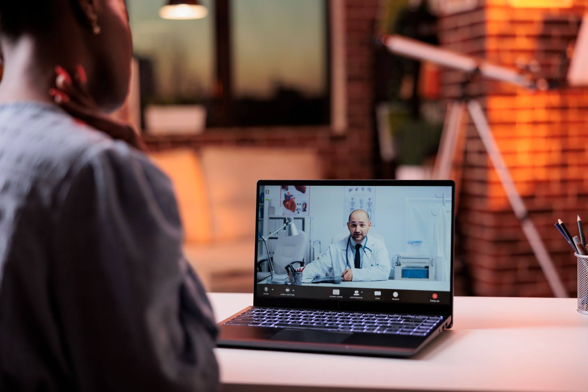Mulher com a mão no pescoço, indicando dor, em consulta virtual com médico via notebook.