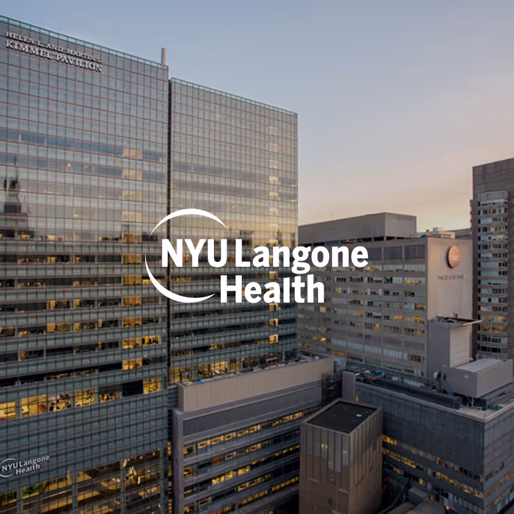 Exterior view of NYU Langone Health hospital buildings at dusk with lit windows and clear sky.